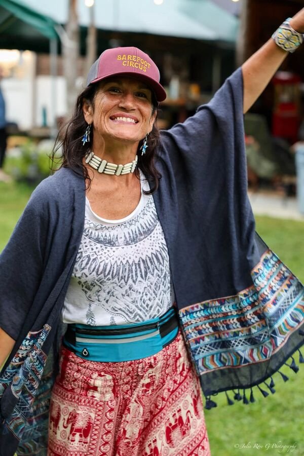 A woman in layered prints with her arms thrown wide, laughing