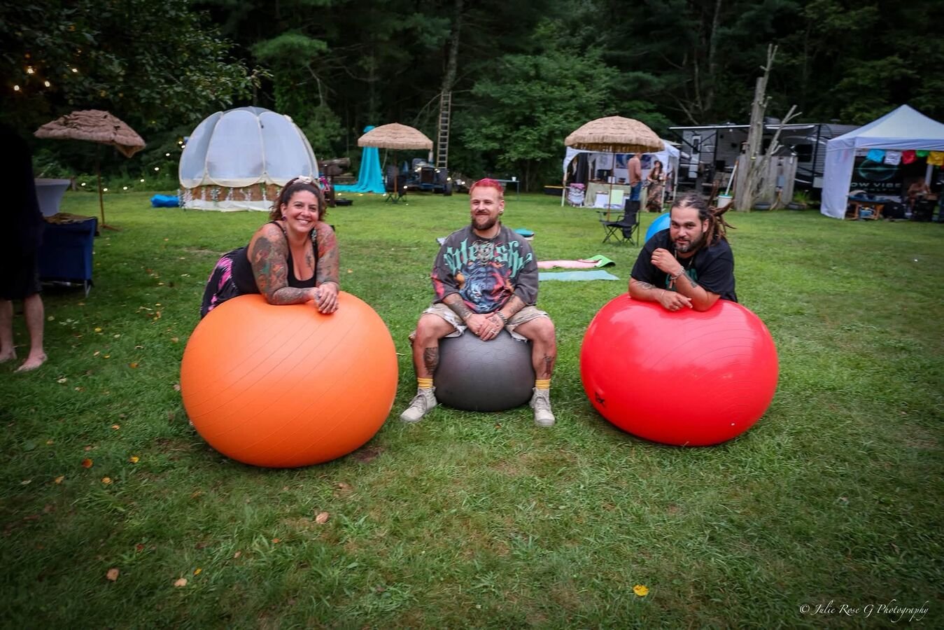 Three people resting on exercise balls on the lawn, bell tents behind