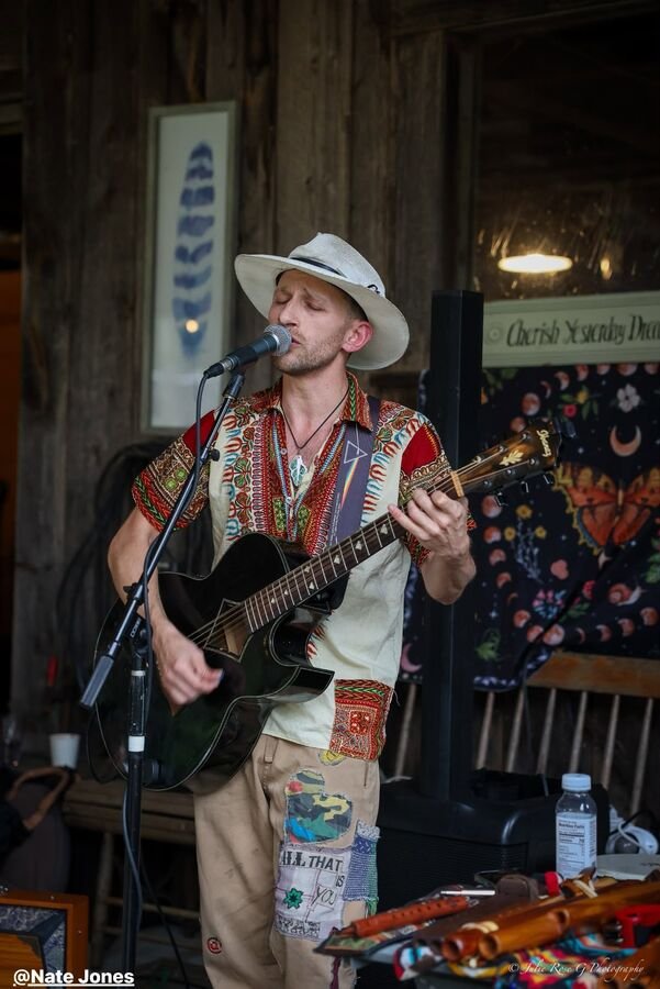 A musician in a wide-brimmed hat playing guitar into a microphone