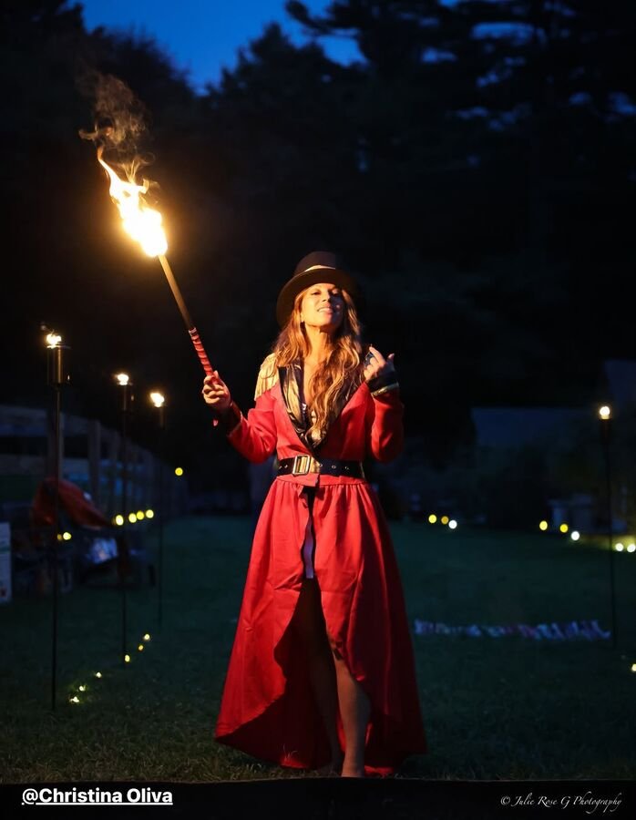A fire performer in a red dress turning a lit torch after dark