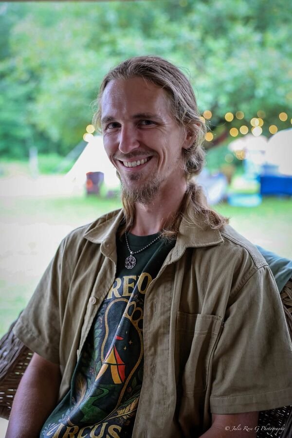A man in a Barefoot Circus shirt smiling into the trees